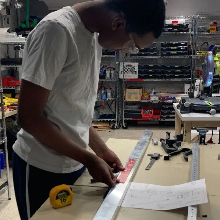 Zach '25 measuring and marking up a 2 by 1 metal tube before cutting it.